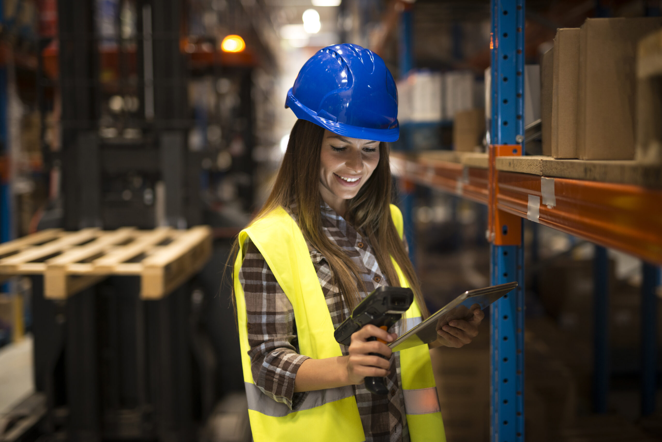 Smiling female worker holding tablet and bar code scanner checking inventory in distribution warehouse.